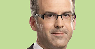 Mann mit schwarzer Brille und grauem Haar schaut leicht lächelnd in die Kamera